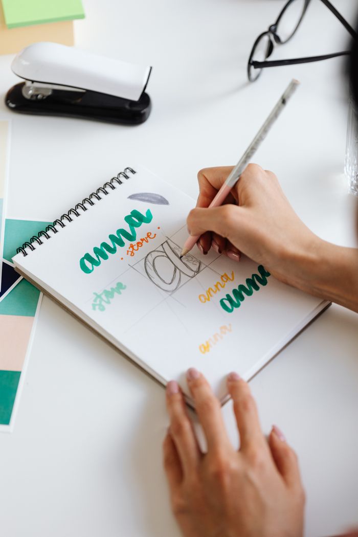 Close-up of creative handwriting practice in a spiral notebook on a designer's desk.